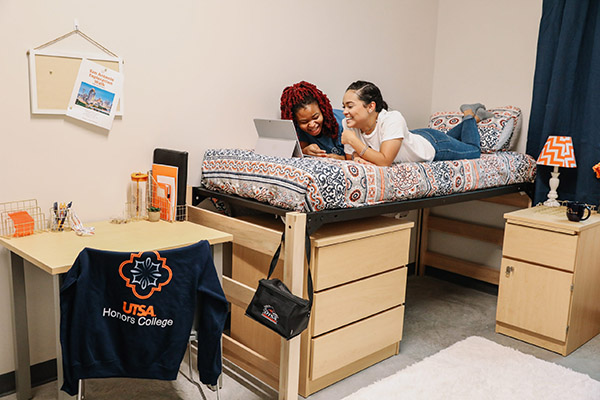 Two smiling students in their bedroom looking at a tablet